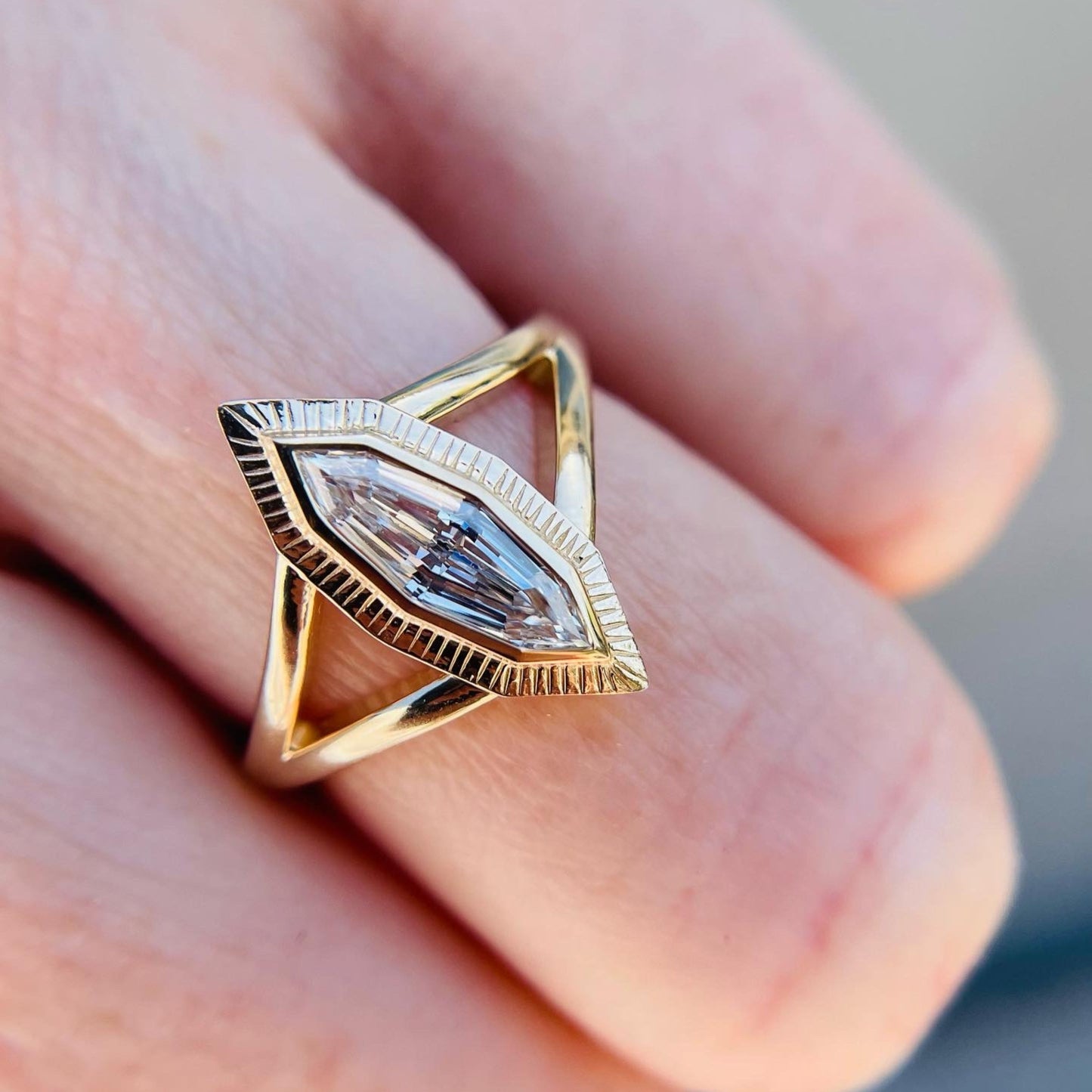 A marquise-cut diamond ring with a triangular gold band rests on a person's finger. The setting is intricate, with a modern, elegant design.