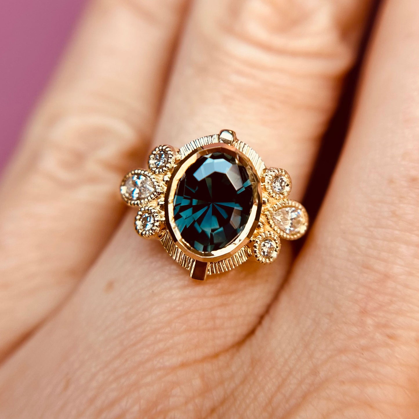 A 14k gold ring with an intricate design features a large, dark blue oval sapphire surrounded by smaller diamond stones, worn on a finger.