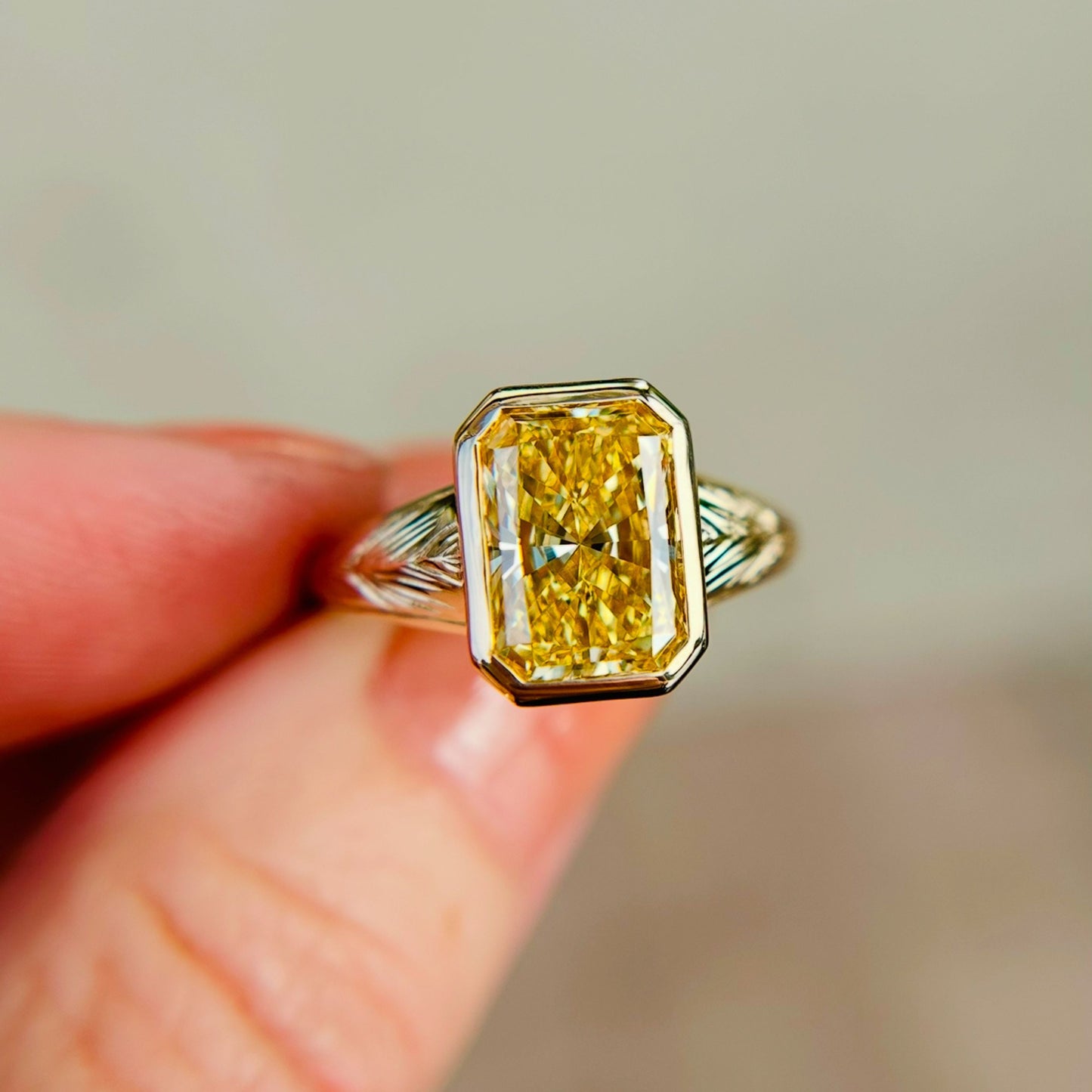 A close-up of a ring with a radiant-cut yellow diamond set in a detailed 14k yellow gold band. The image conveys luxury and elegance against a soft background.