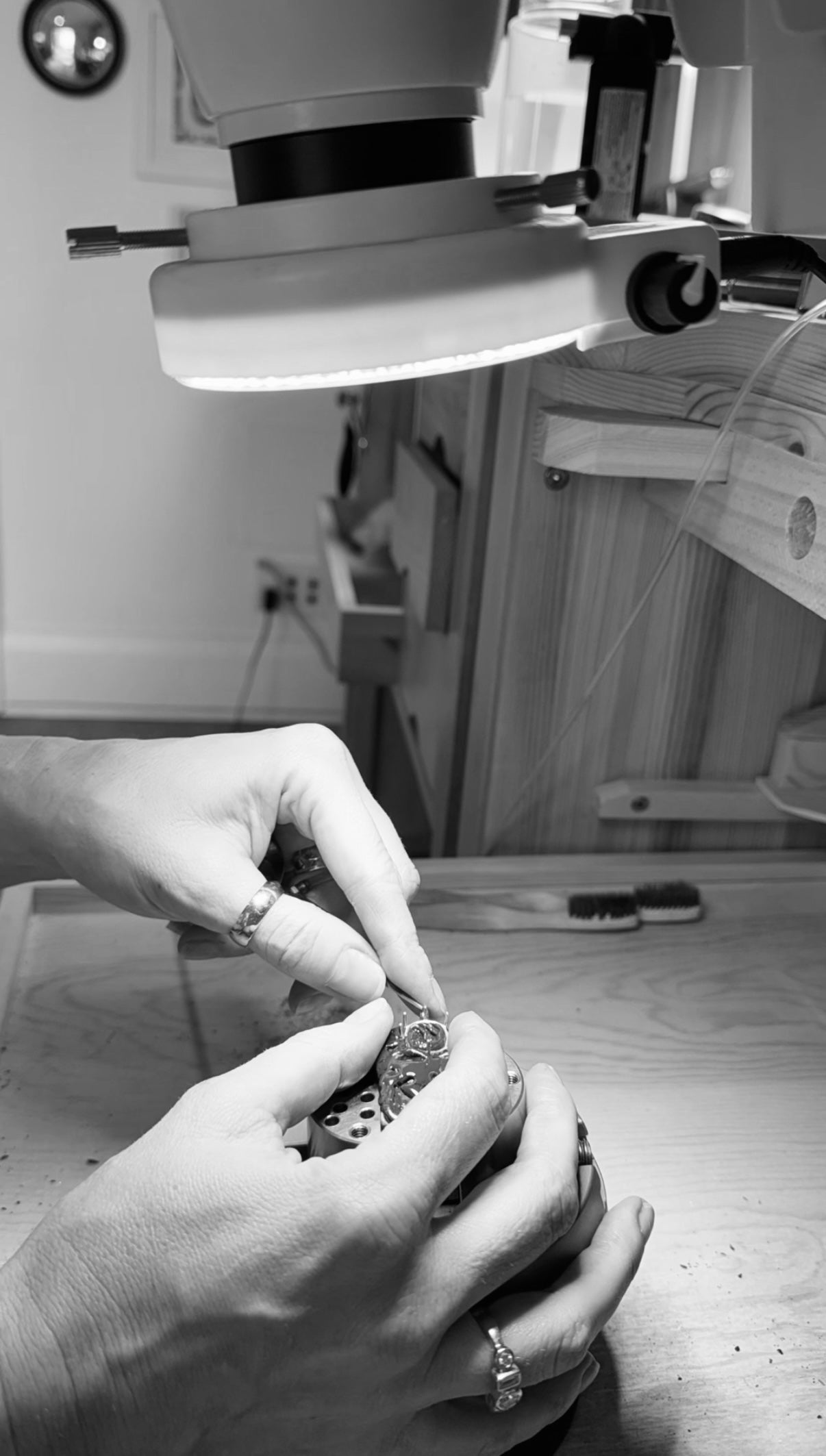 Jilian Maddin's hands wearing rings working on a detailed piece under a magnifying light in her Toronto studio, conveying precision and craftsmanship in a focused setting. The image is in black and white.