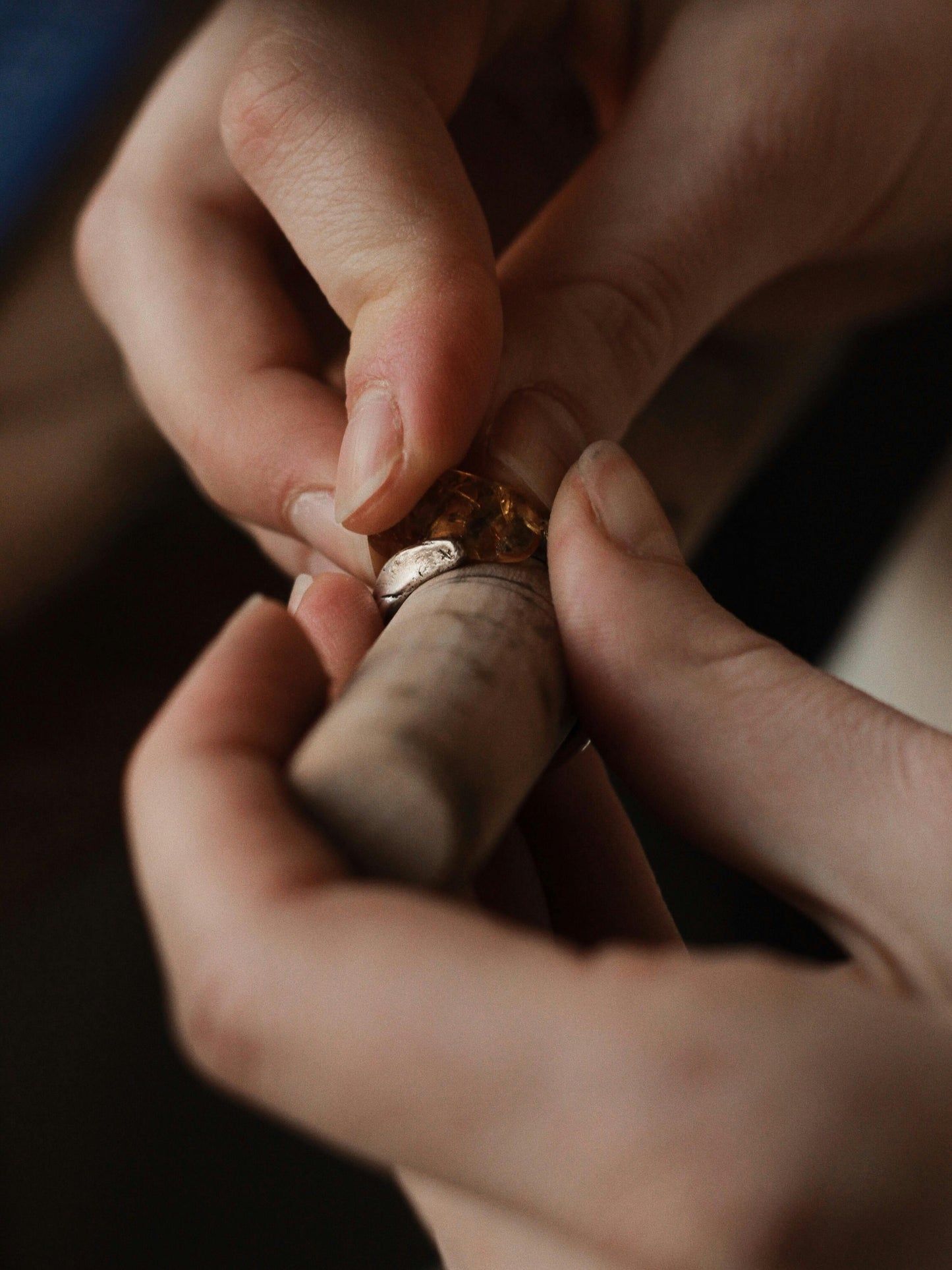 Two hands carefully set a stone into a gold ring on a mandrel. The focus is on the delicate craftsmanship, evoking a sense of precision and artistry.