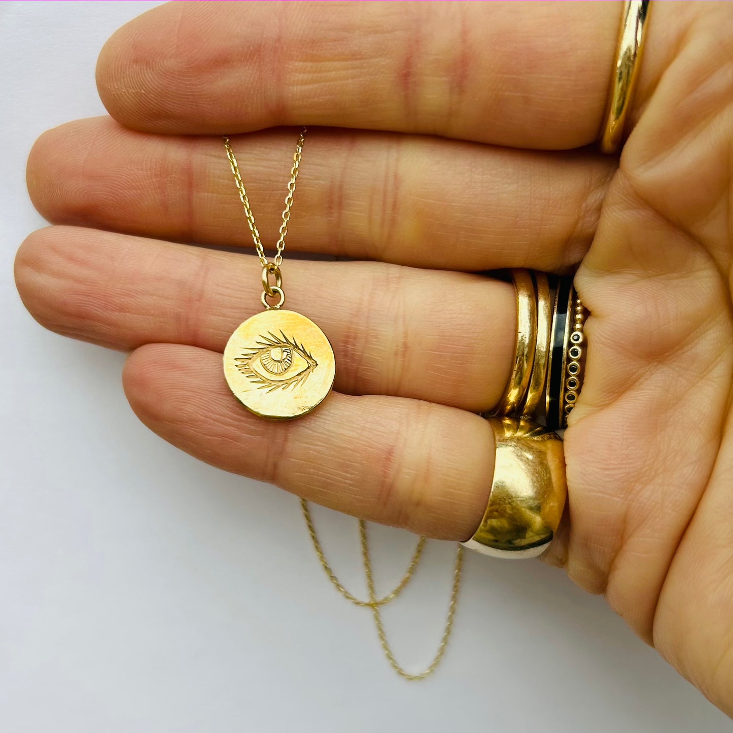 A hand holding a 10K yellow gold pendant necklace on a cable chain with a hand-carved eye design.