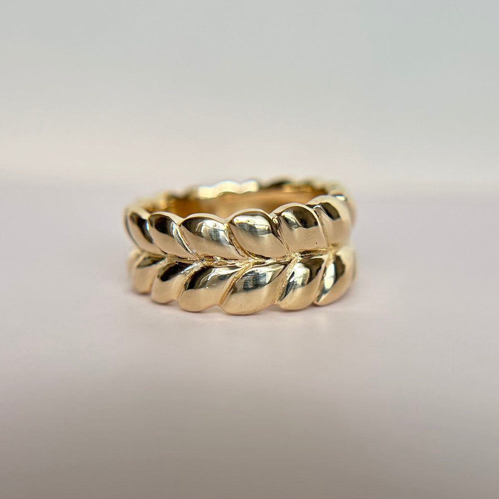 
                  
                    An organically shaped braided wedding band in 14K yellow gold, lays on a white surface.
                  
                