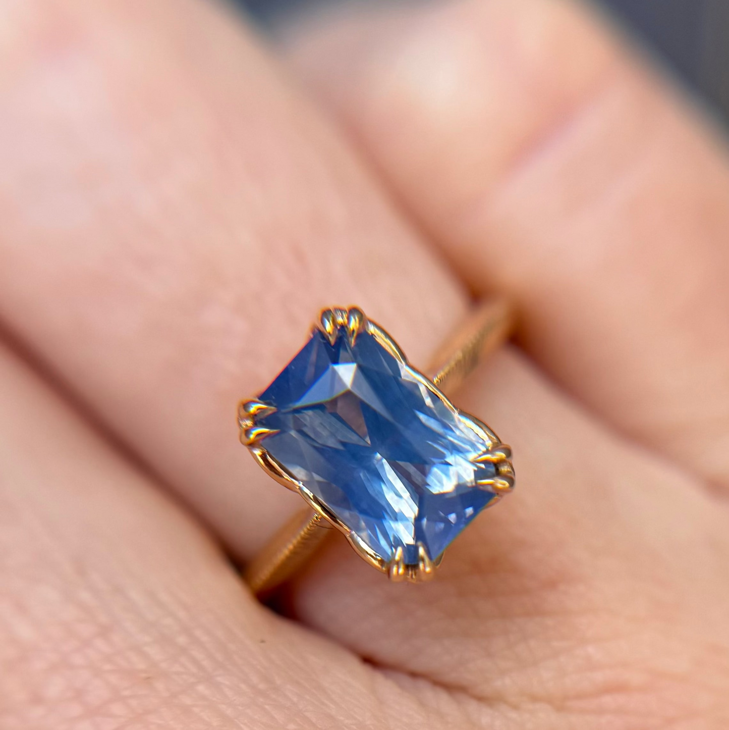 Yellow Gold classic solitaire engagement ring with a unique blue sapphire gemstone worn on a person's finger