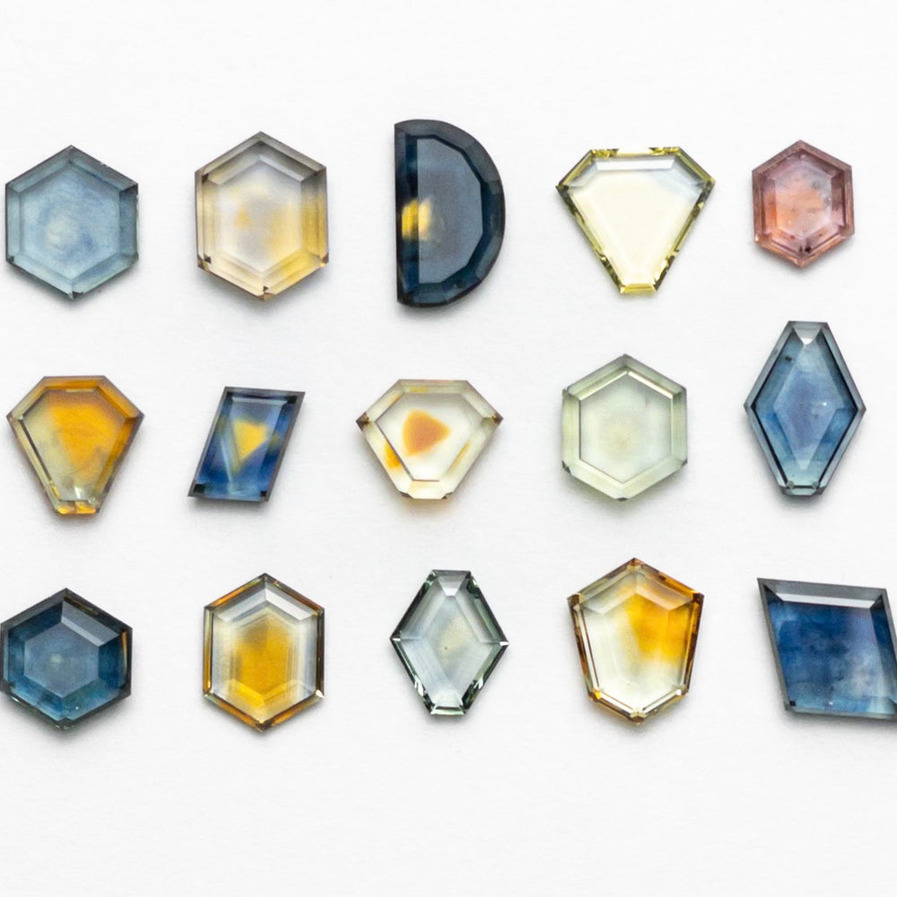 A collection of colorful, multi-shaped gemstones is arranged neatly on a white background. The stones are in hexagonal, octagonal, and half-circle shapes, featuring hues of blue, yellow, pink, and orange, creating a vibrant visual display.