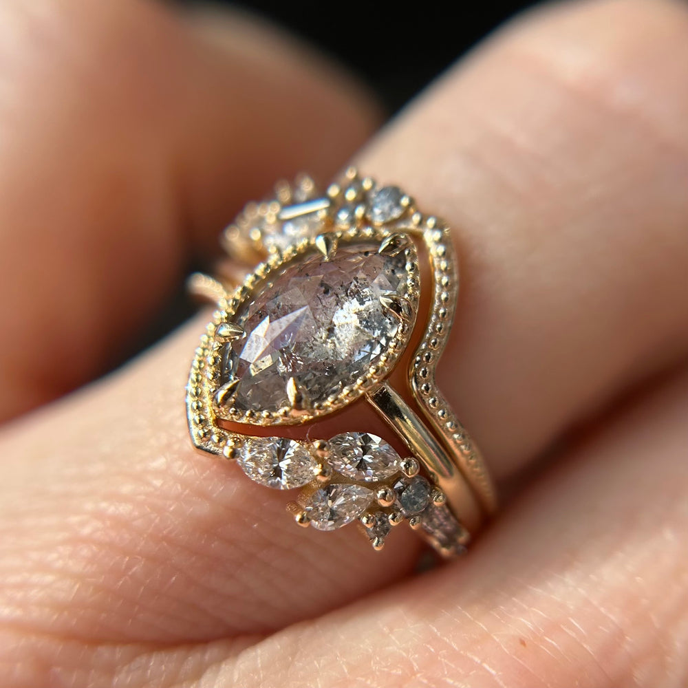A close-up of an elegant gold ring featuring a large marquise-cut diamond in the center, stacked with two unique wedding bands either side with diamonds.
