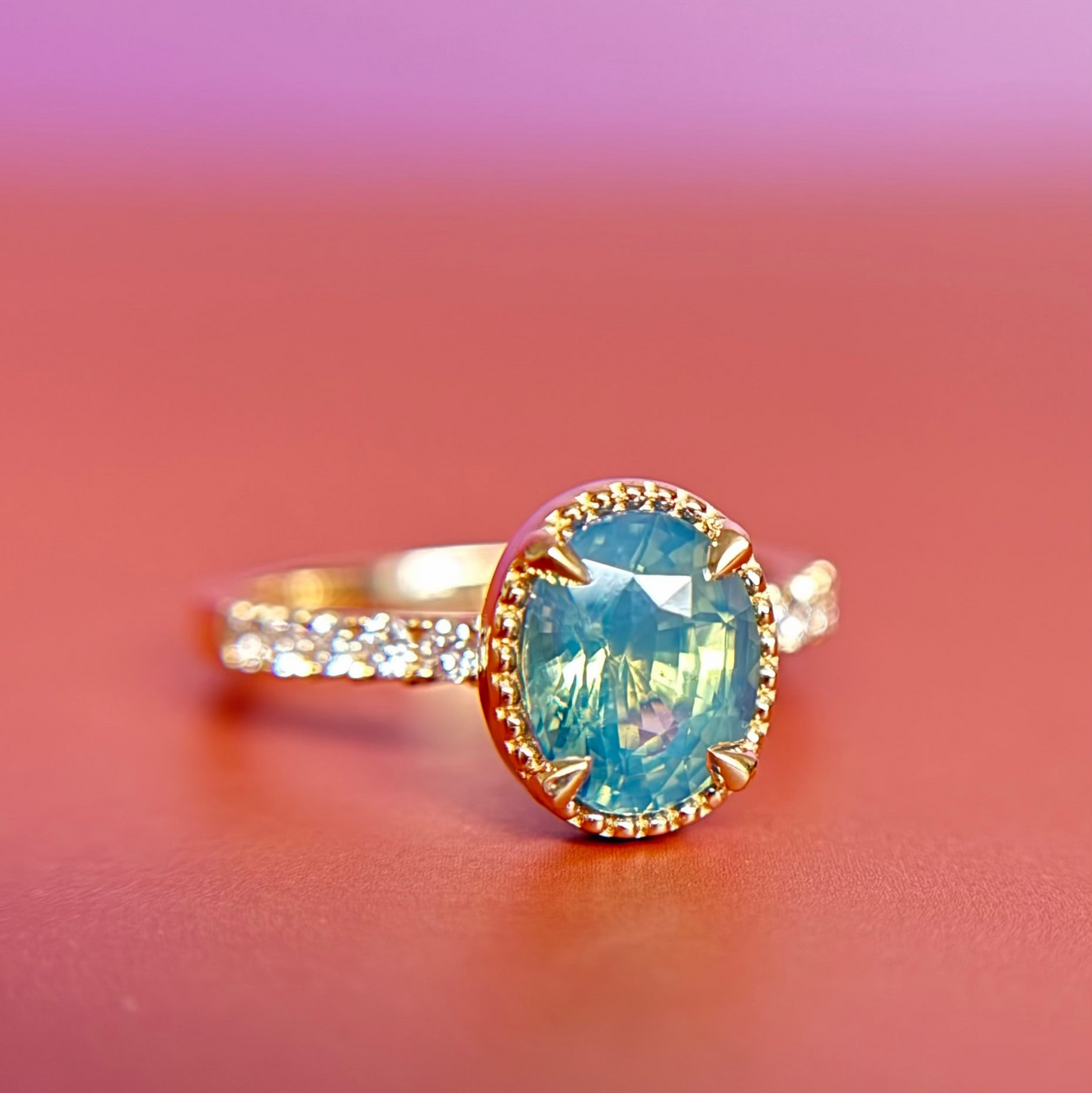 Yellow Gold engagement ring with a large teal oval gemstone, the light makes it glow on a gradient background