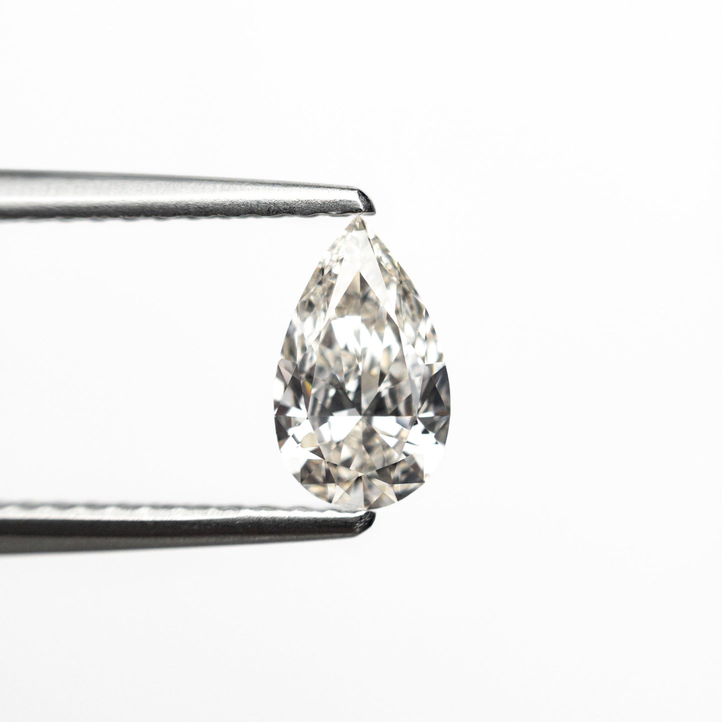 A pear-shaped diamond, held by tweezers, sparkles against a plain white background, highlighting its clarity and intricate facets.