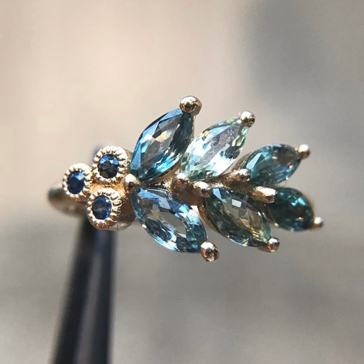 Elegant ring featuring marquise-cut blue gemstones arranged in a leaf pattern, accented by small round dark blue sapphires on a gold band; exudes sophistication and artistry.