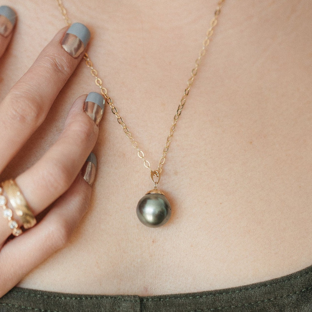 
                  
                    A grey pearl pendant necklace on a 18-inch long yellow gold round cable chain, displayed on a person's neck.
                  
                