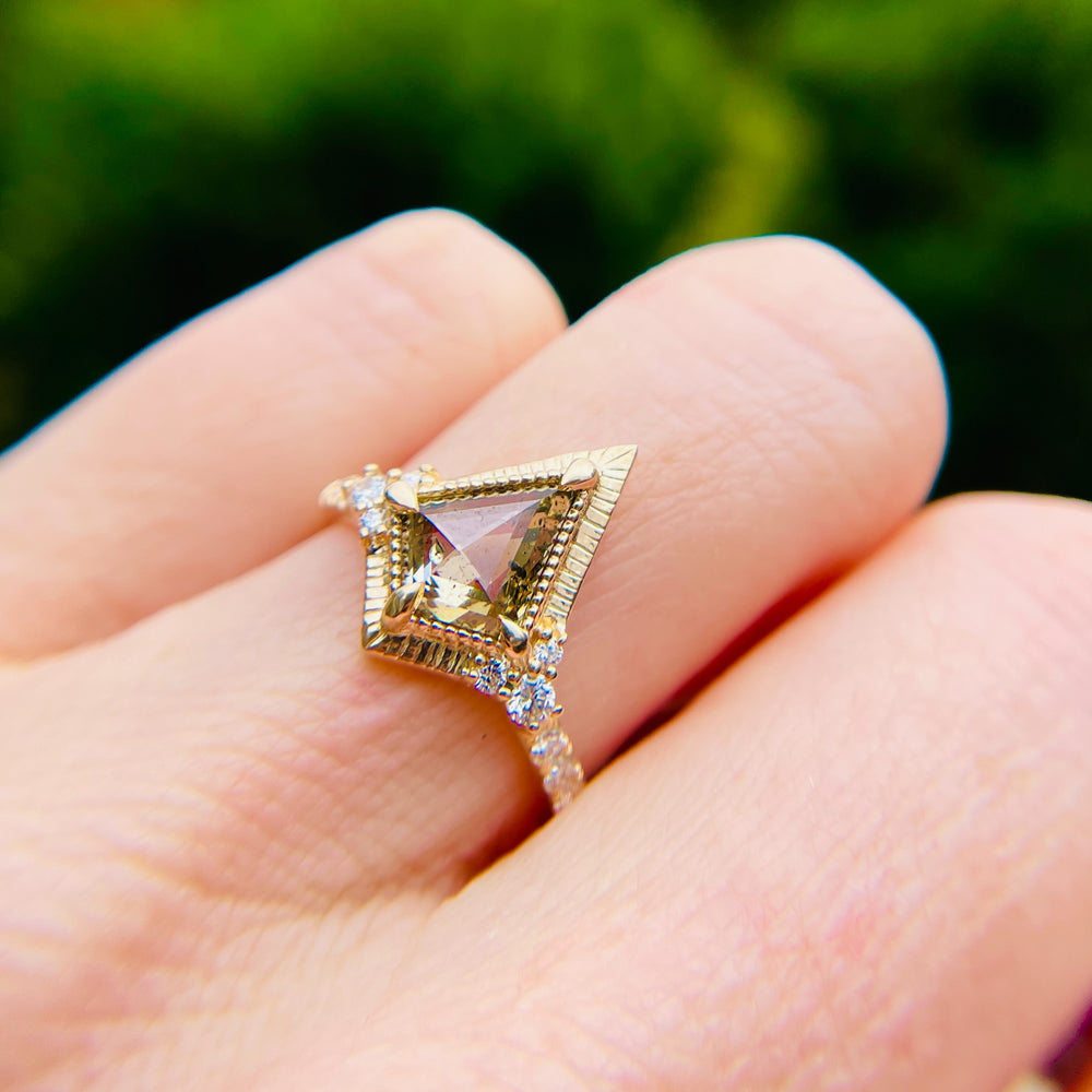 
                  
                    A hand displays a yellow gold ring with a large, kite-shaped yellow diamond in the center, surrounded by small sparkling diamonds, set against a blurred green background.
                  
                